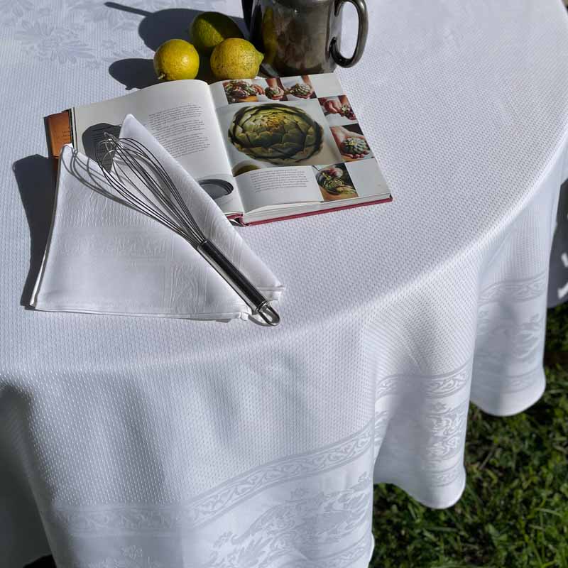 Edge of a white round jacquard woven tablecloth with matching napkins and table decorations