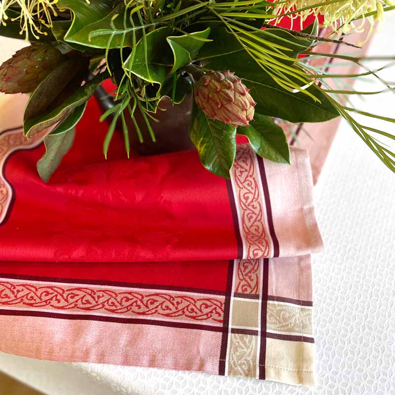 Decorative table setting with a red and gold tablecloth and green foliage.