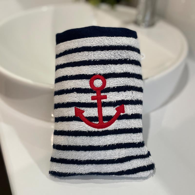 A washcloth bath mitt with navy and white horizontal stripes and a red anchor motif, placed on a white sink countertop.
