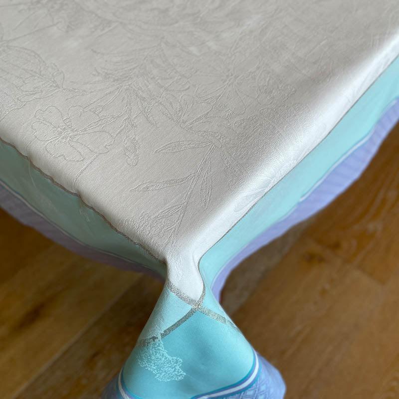 Corner detail of Biarritz Aqua Purple jacquard tablecloth showing white floral top.