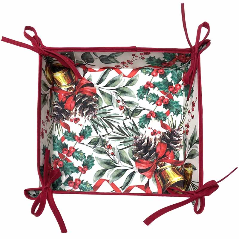 A square bread basket featuring a festive Christmas print with holly leaves, pinecones, red ribbons, and gold bells on a white background, finished with red ties.