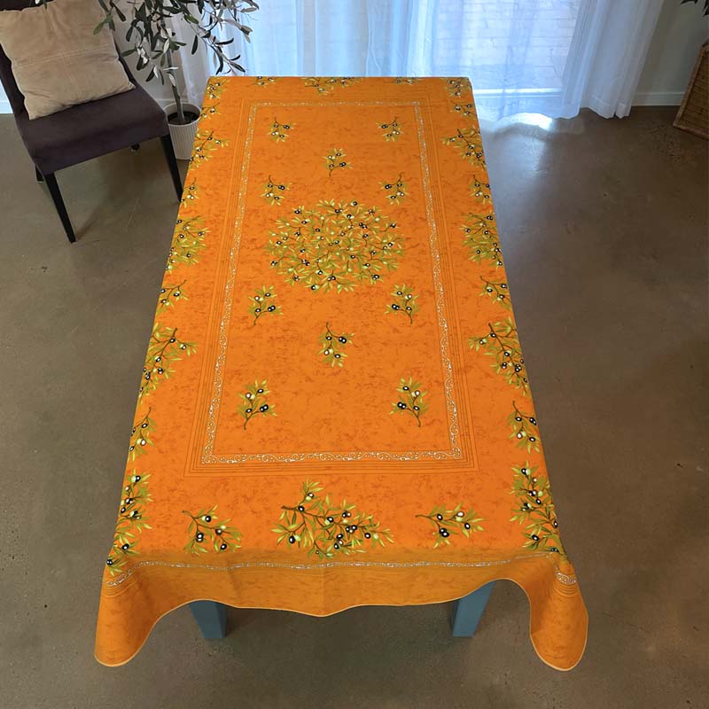 Orange tablecloth with floral patterns on a wooden table in a room.