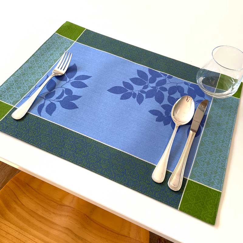 Blue and green patterned placemat with cutlery on a white table.