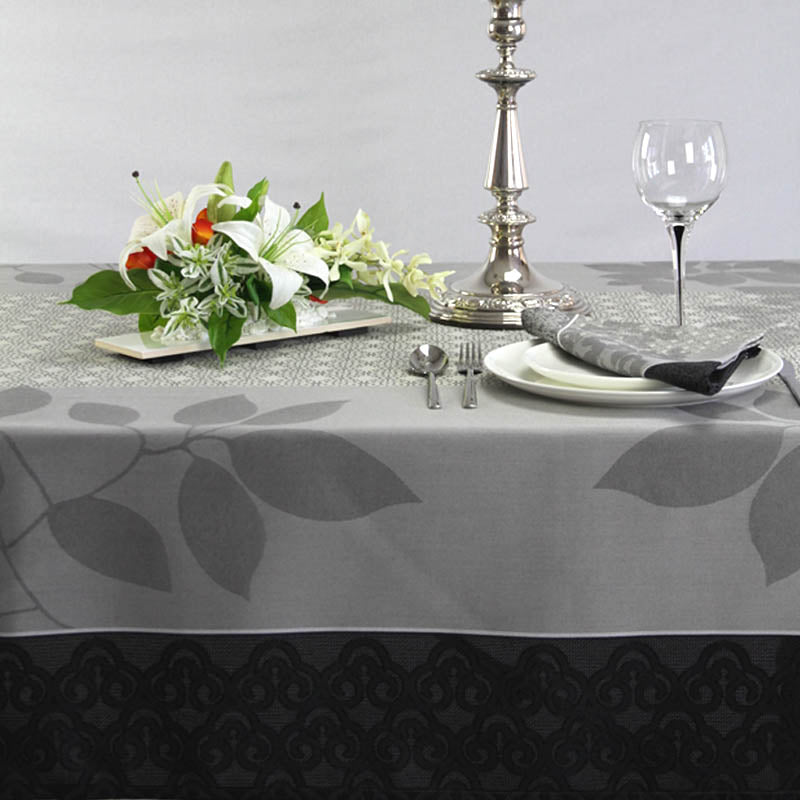 Dining table setting with floral centerpiece, silver candle holder, and glassware on a gray leaf-patterned tablecloth.