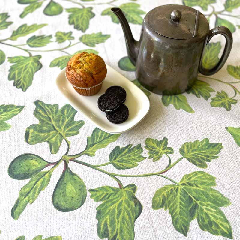 Tea set with teapot, muffin, and cookies on a leaf-patterned tablecloth