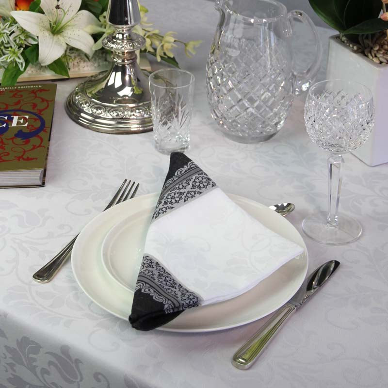 Dining table setting with plates, cutlery, and decorative items on a white tablecloth.