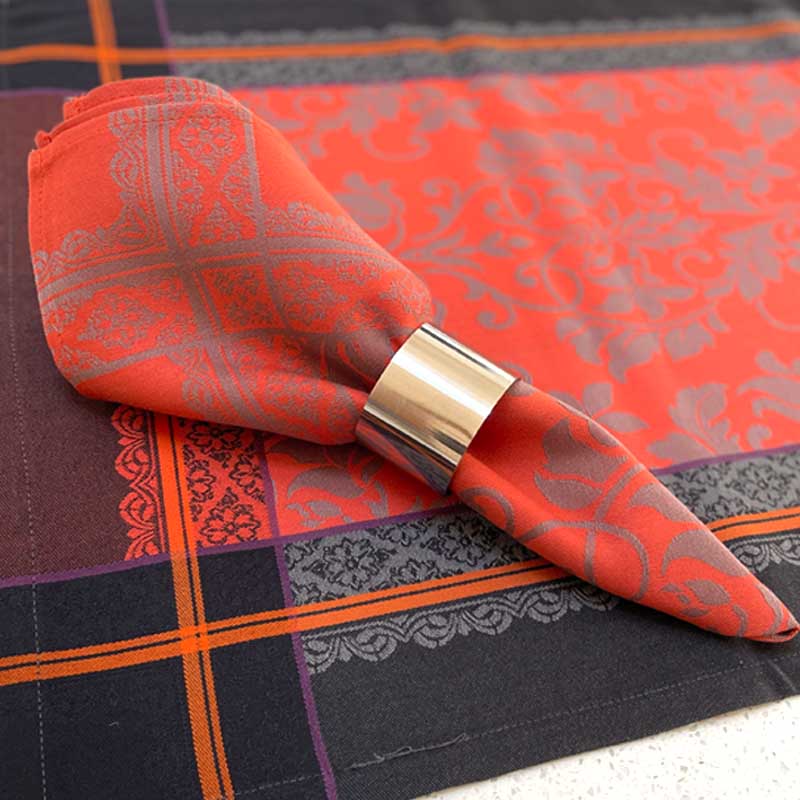 Orange patterned napkin with a gold napkin ring on a tablecloth.