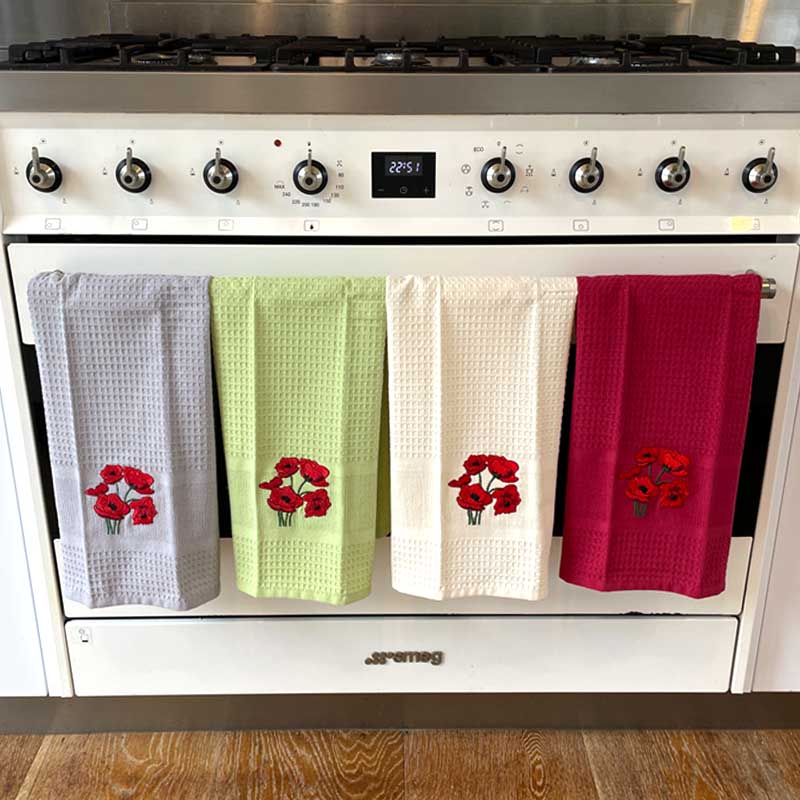Four colorful kitchen towels with floral designs hanging on a white stove.