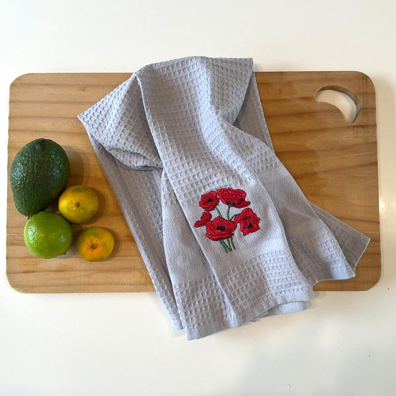 Gray towel with red floral embroidery on a wooden cutting board with fruits