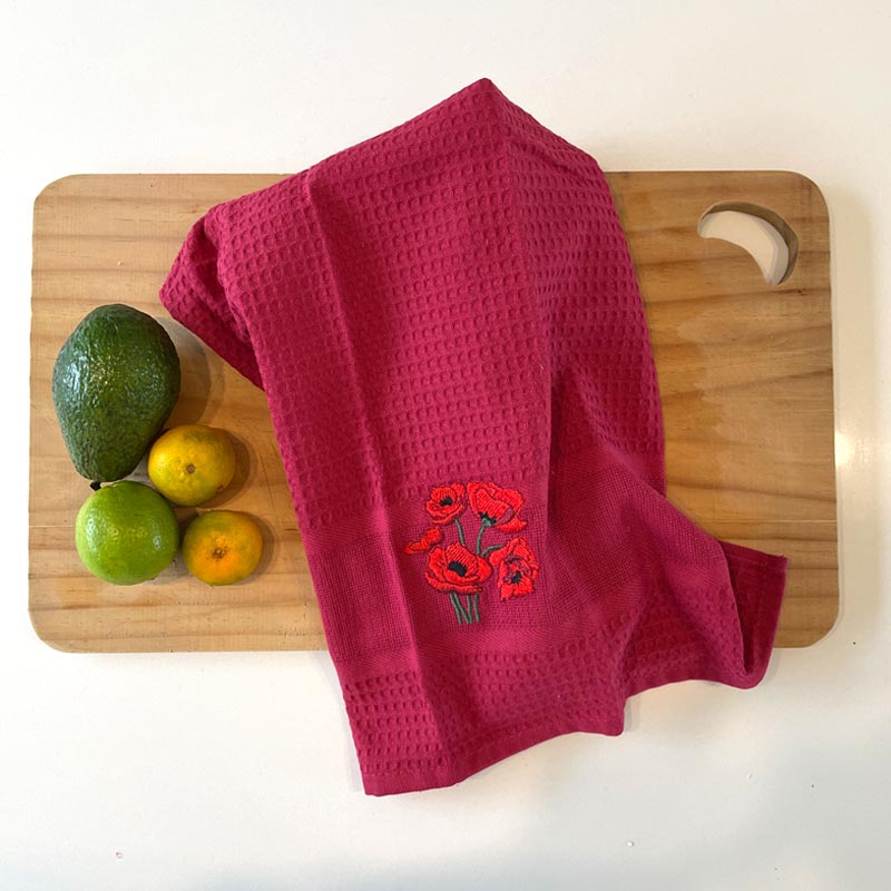 Red towel with floral embroidery on a wooden cutting board with fruits