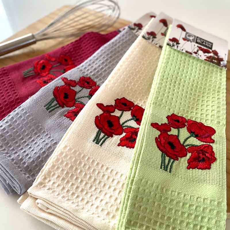 Set of embroidered kitchen towels with red floral designs on a wooden surface.