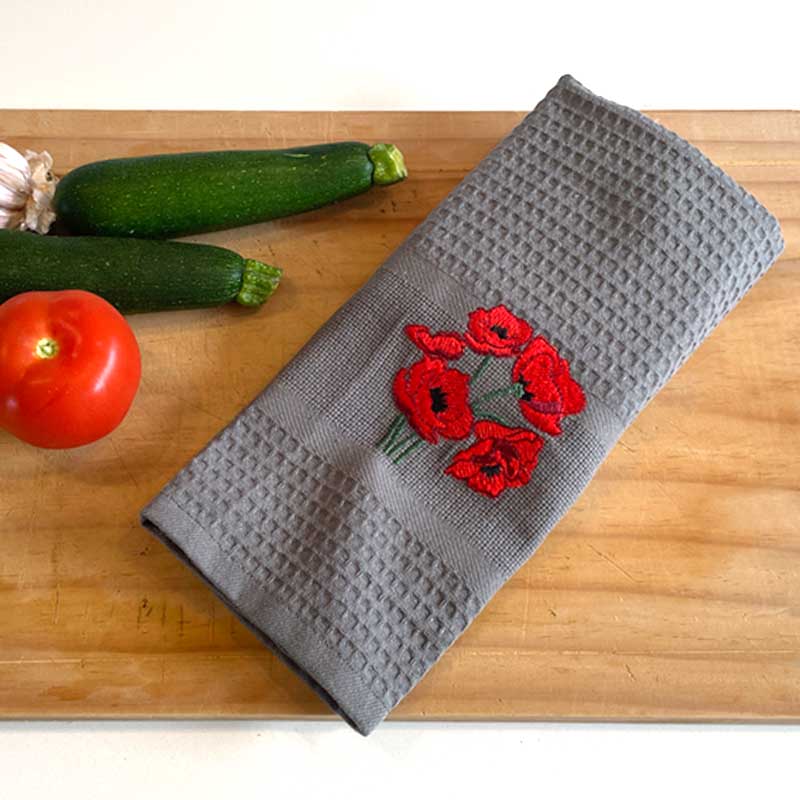 Gray towel with red floral embroidery on a wooden surface with vegetables.