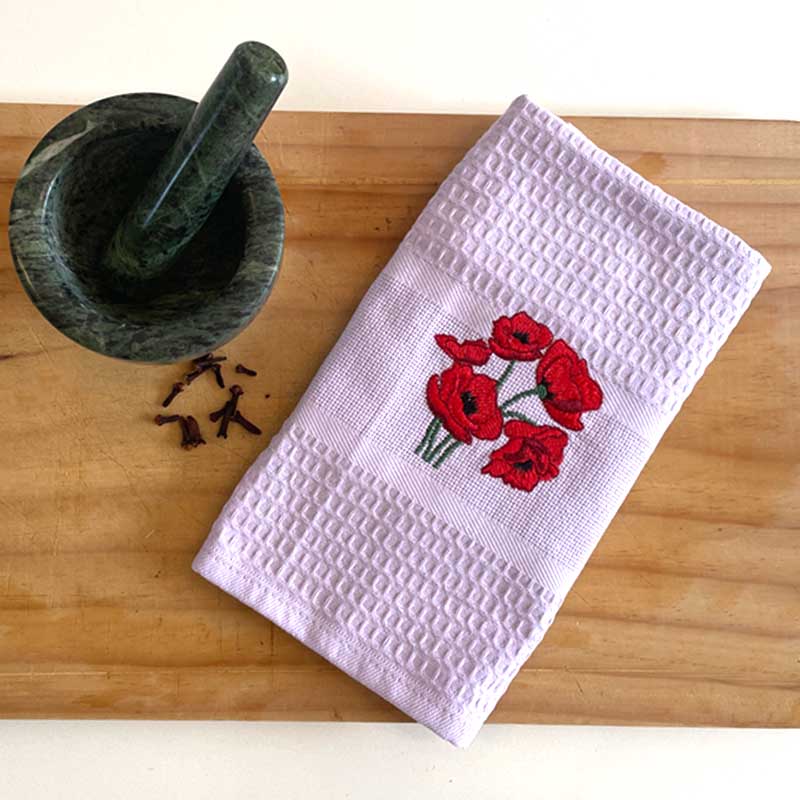 White towel with red floral embroidery on a wooden surface next to a green mortar and pestle.