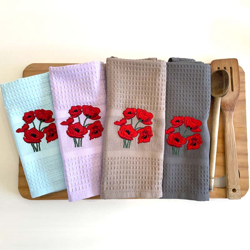 Four kitchen towels with red floral designs on a wooden board.