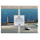 A rectangular boxed fragrance product shown against a plain white background. The box features a coastal illustration with a lighthouse, boats, shoreline, and a central label reading 'Savons de Marseille' and 'Aloe Vera - Coton Fleurs - Patchouli - Rose'.