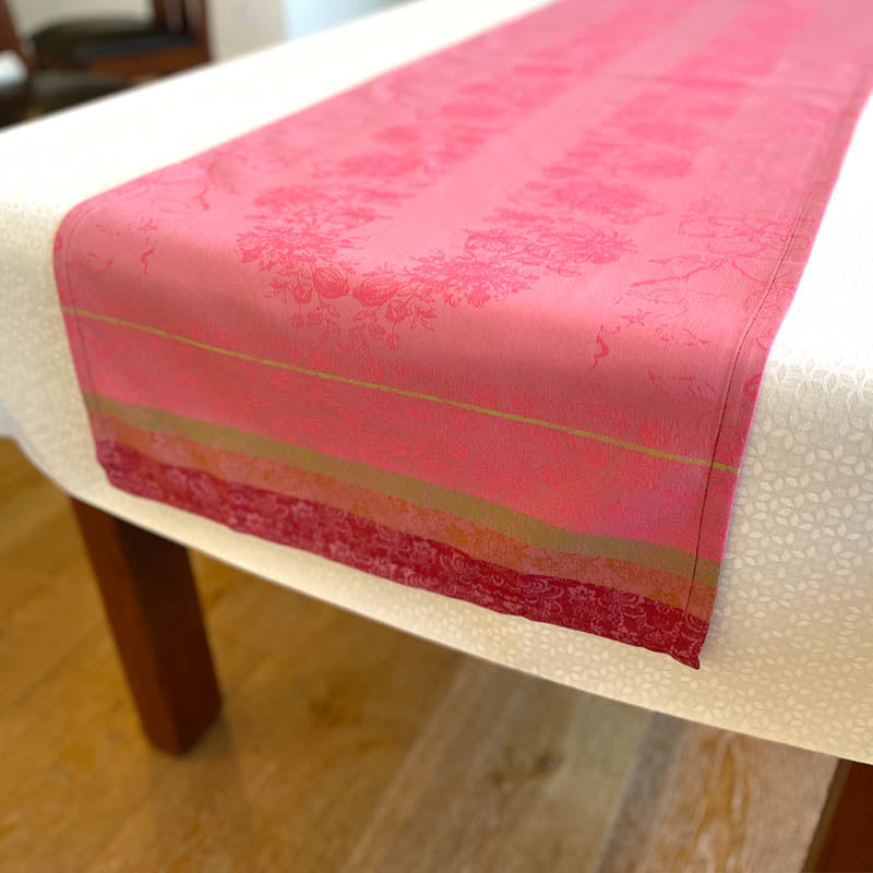 Pink patterned table runner on a white tablecloth with wooden legs.