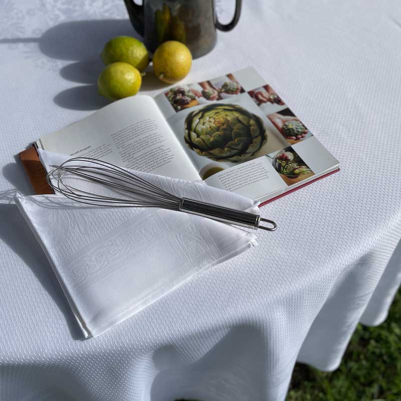 Open cookbook with a whisk and napkin on a white tablecloth outdoors