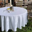 Round table with a white tablecloth, lemon, teapot, and magazine in an outdoor setting.