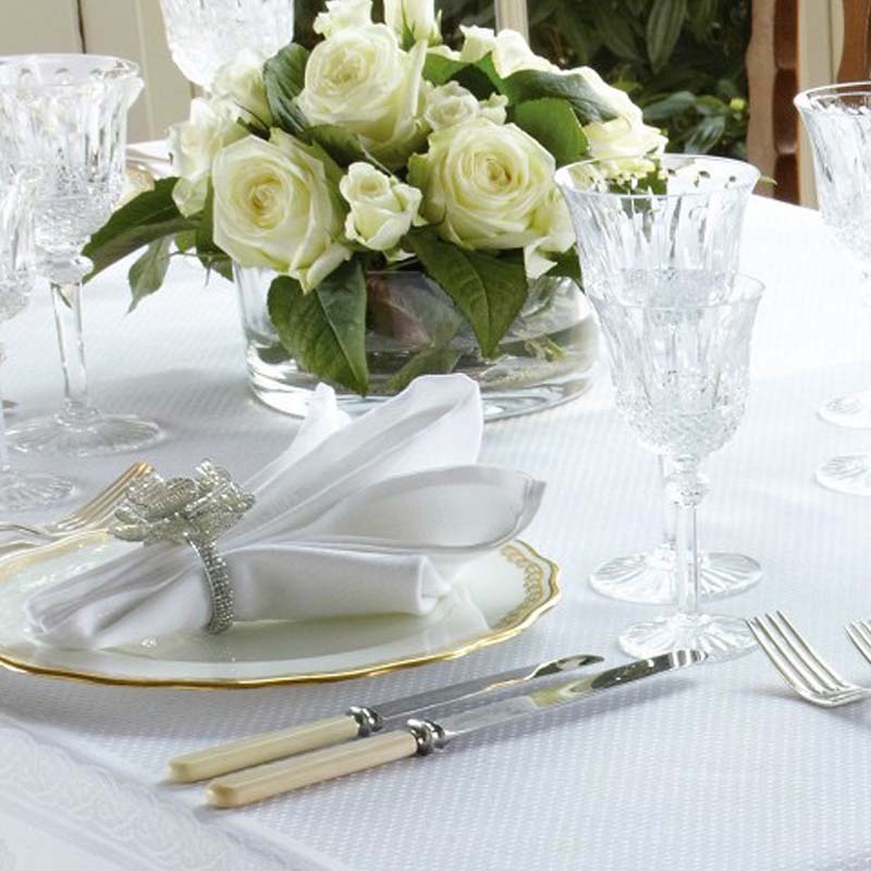 Elegant table setting with white napkins, roses, cutlery, and glasses on a white tablecloth.