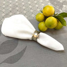 White jacquard napkin with a decorative napkin ring on a gray tablecloth with lemons