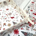 A close-up of a white bread basket in festive Christmas patterned fabric with red, gray, and beige holiday motifs, tied with a cream ribbon.
