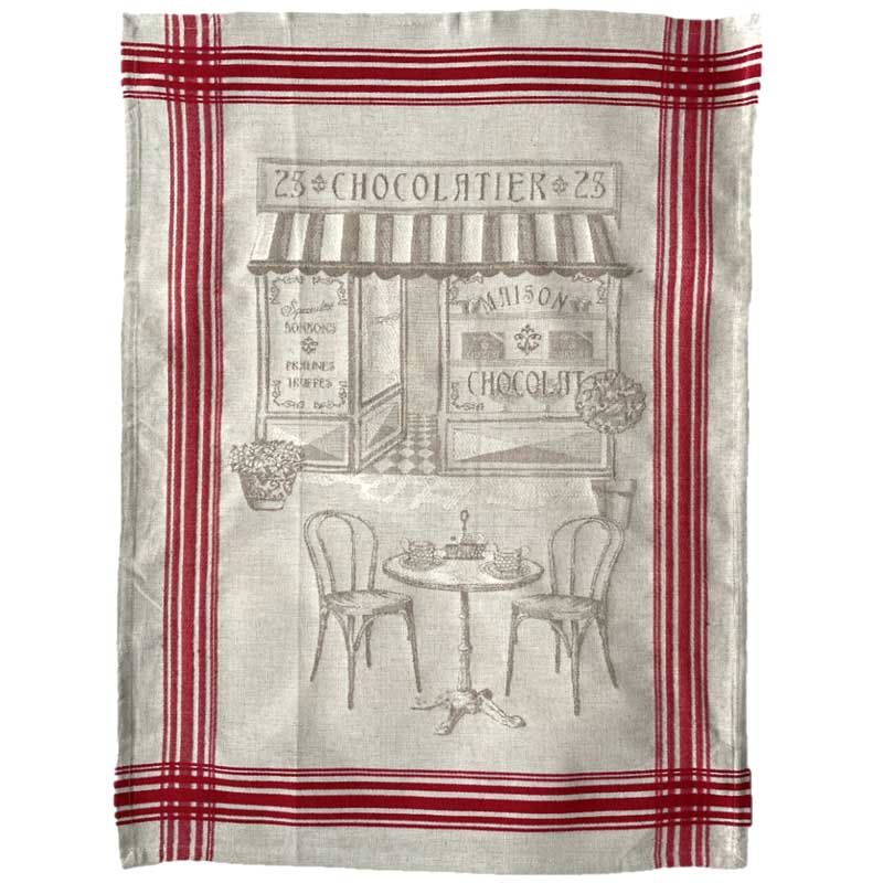 A rectangular kitchen tea towel with a red and beige plaid border and a central illustration of a vintage French cafe storefront labeled '23 CHOCOLAIER 23', featuring a small table and chairs.