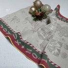 A Christmas tea towel with a festive border and subtle holiday motifs, styled on a white speckled countertop with decorative ornaments.