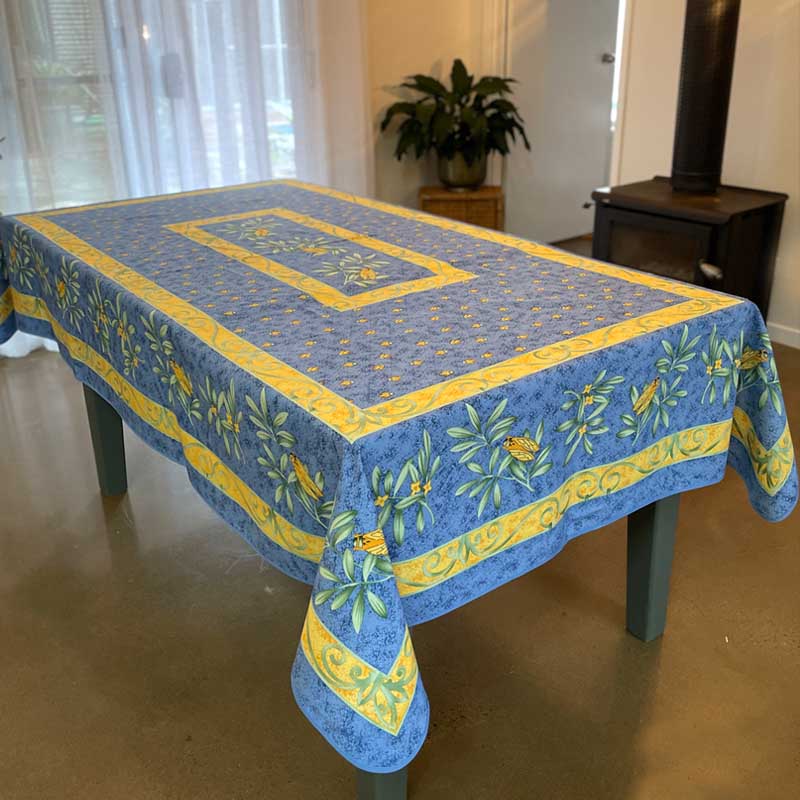 Blue and yellow patterned tablecloth on a table in a room with curtains and a plant.