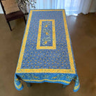 Blue tablecloth with yellow border on a wooden table in a room.
