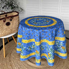 Round blue tablecloth with yellow and green patterns on a round table, next to a woven basket.