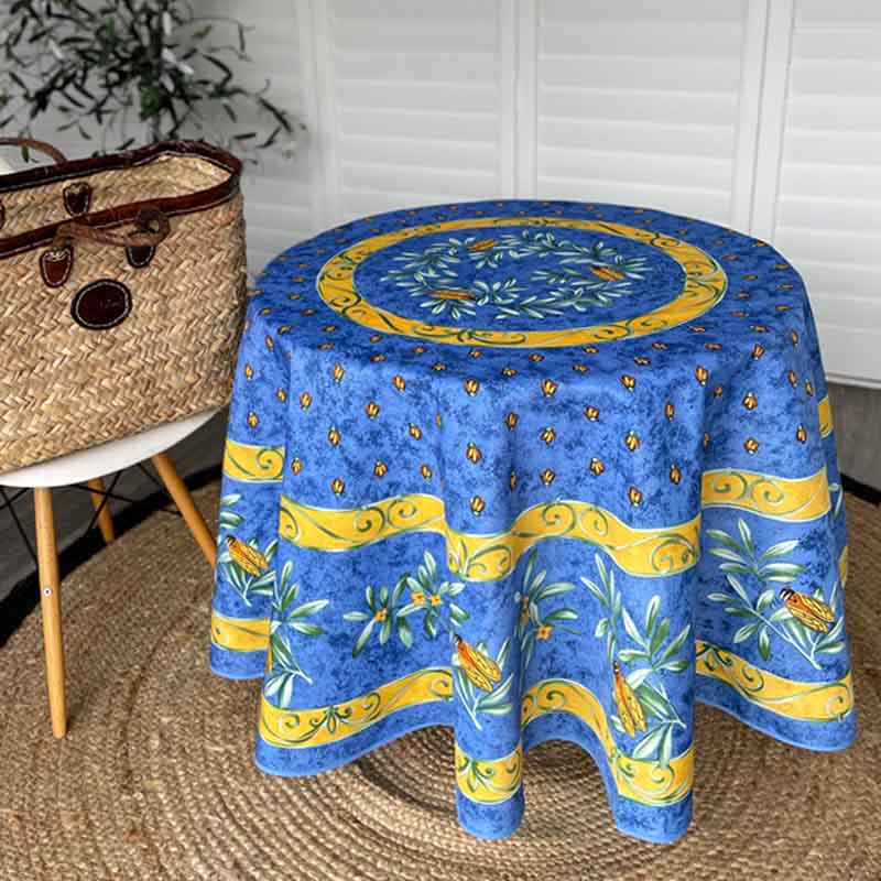 Round blue tablecloth with yellow and green patterns on a round table, next to a woven basket.