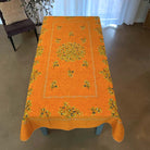 Orange tablecloth with floral patterns on a wooden table in a room.