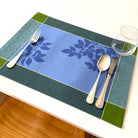 Blue and green patterned placemat with cutlery on a white table.