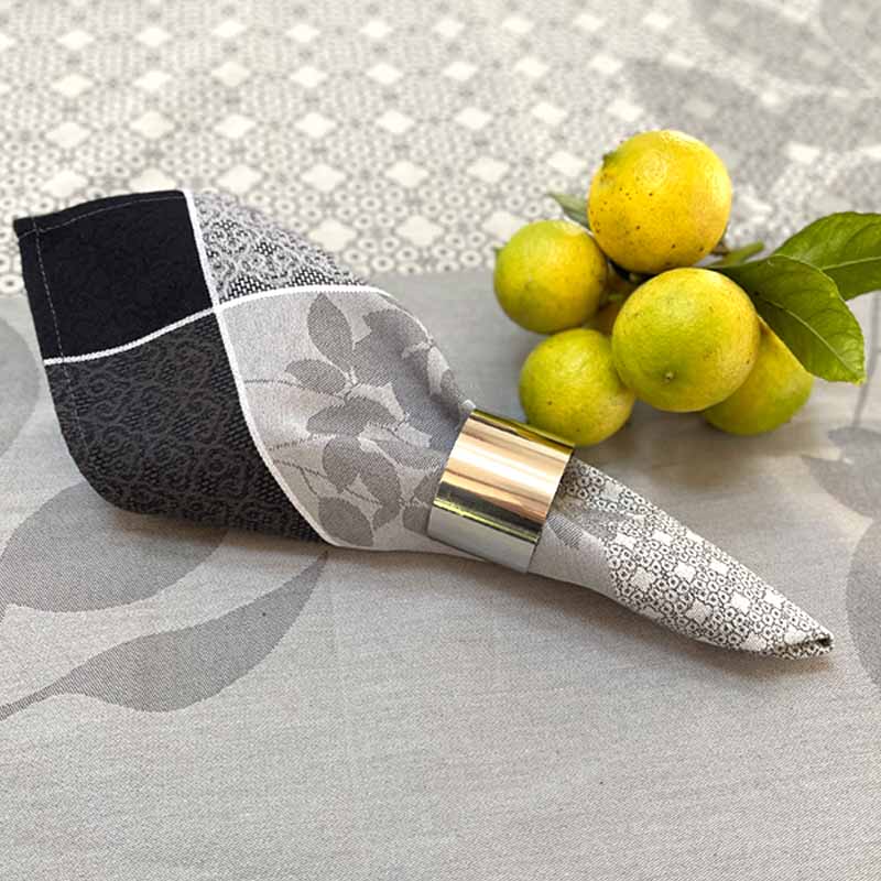 Decorative jacquard napkin with  silver napkin ring on a tablecloth with lemons.