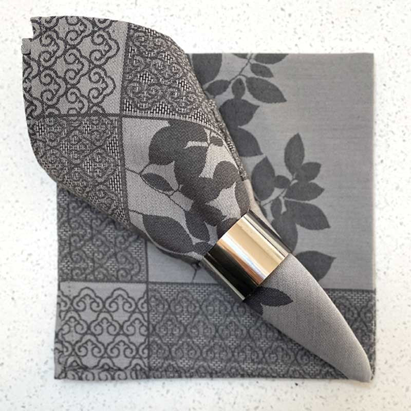 Decorative jacquard napkin with floral pattern and silver holder on a textured surface