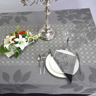 Dining table setting with floral arrangement, silver candlestick, and cutlery on a gray leaf-patterned tablecloth.