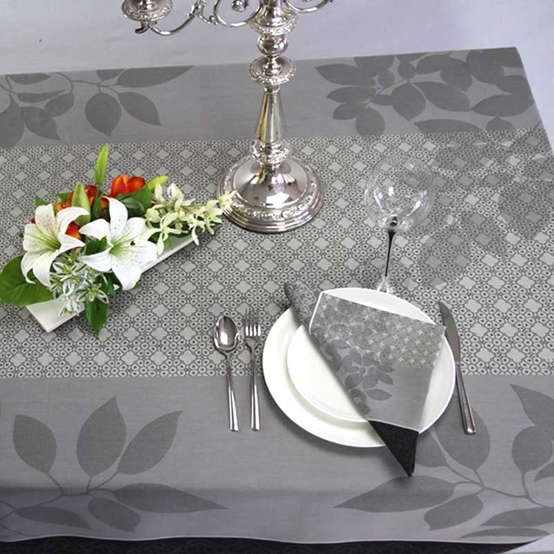Dining table setting with floral arrangement, silver candlestick, and cutlery on a gray leaf-patterned tablecloth.