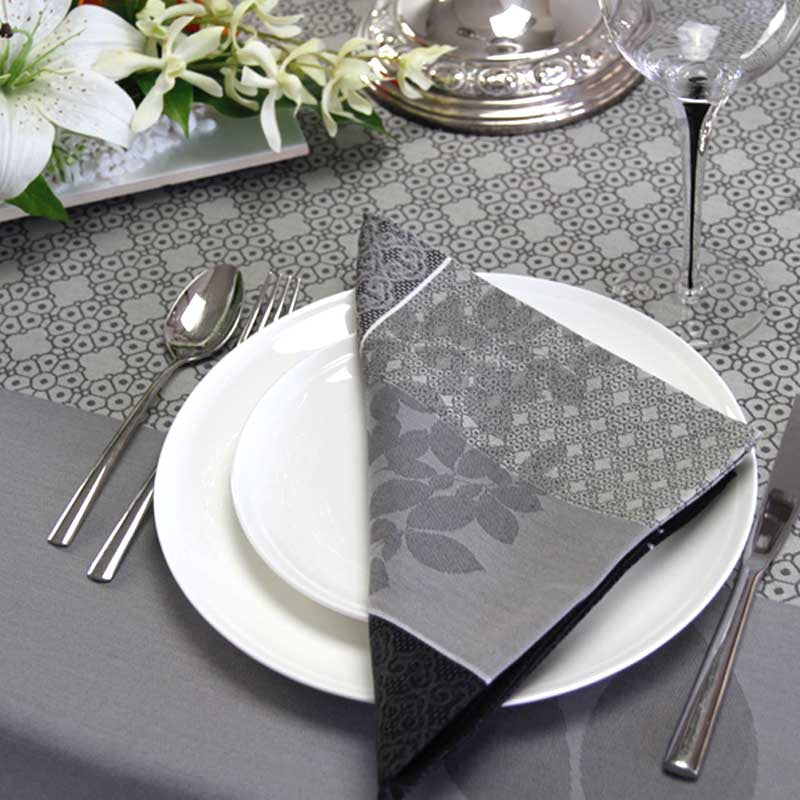 Elegant table setting with floral napkin, silverware, and patterned tablecloth.