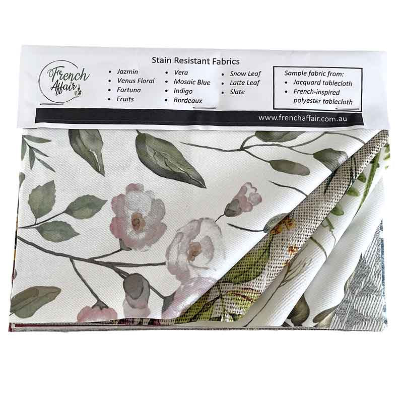 A folded piece of French Affair stain resistant tablecloth fabric with a floral print, shown with its white paper header card containing product details and a list of stain resistant options.