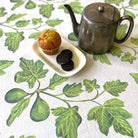 Tea set with teapot, muffin, and cookies on a leaf-patterned tablecloth