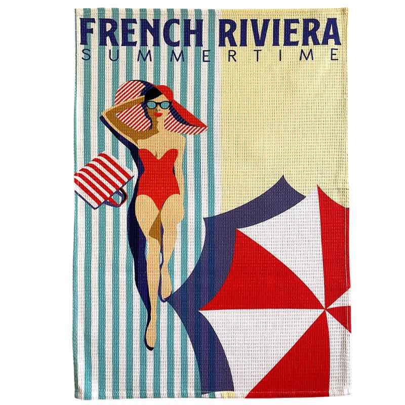 A waffle-weave tea towel featuring a retro French Riviera summer beach illustration with the text 'FRENCH RIVIERA SUMMERTIME' at the top, a woman in a red swimsuit and striped hat, and a red, white, and navy umbrella on a cream background.
