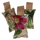Three small hanging lavender sachets with flower and leaf pattern and gold hanging ribbon. On a white background.