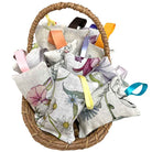 A woven wicker basket filled with multiple lavender sachets featuring floral prints in pink, purple, blue, green, and yellow, each with a ribbon loop at the top, shown on a plain white background.