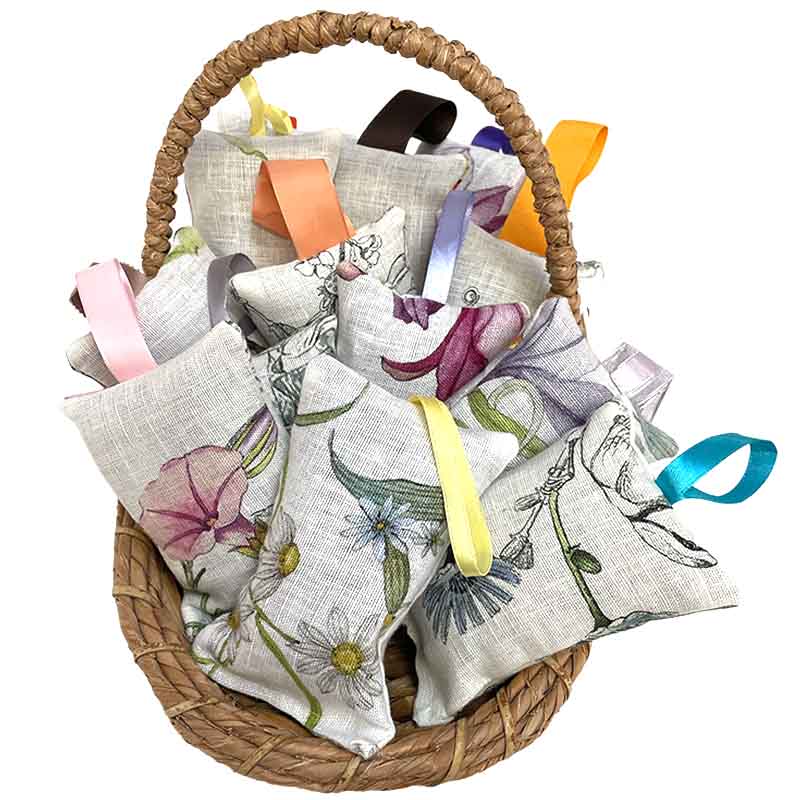 A woven wicker basket filled with multiple lavender sachets featuring floral prints in pink, purple, blue, green, and yellow, each with a ribbon loop at the top, shown on a plain white background.