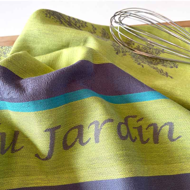 Green and purple striped towel with 'Jardin' text and a whisk on a wooden surface