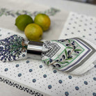 A folded patterned napkin with a metallic silver ring, styled on a white tablecloth with blue dots and olives, with three lemons in the background.