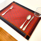 Orange and black patterned placemat with silverware on a white table.