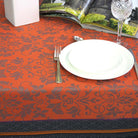 Table setting with an Orange and black jacquard tablecloth, white plate, silver fork, and glass.