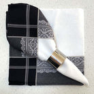 Black and white patterned napkin with silver napkin ring resting on another napkin
