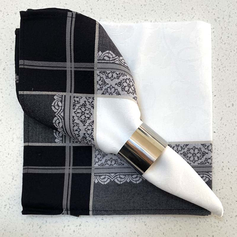 Black and white patterned napkin with silver napkin ring resting on another napkin